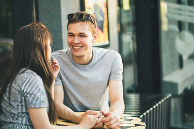 Happy man looking at girlfriend at outdoor cafe in city