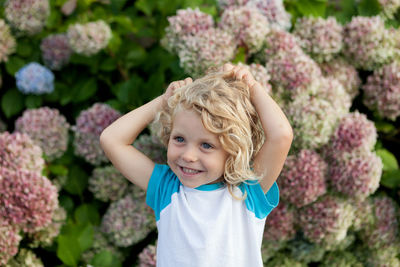 Cute girl with hands in hair standing against plants