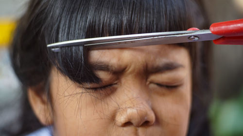 Close-up of scissors cutting girl hair outdoors