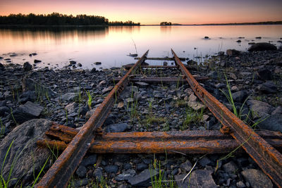 Rusty train tracks descend into a lake at sunset.
