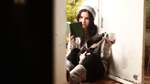 Young woman using mobile phone while sitting on wall