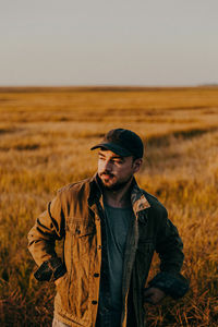 Young man looking away on field against sky