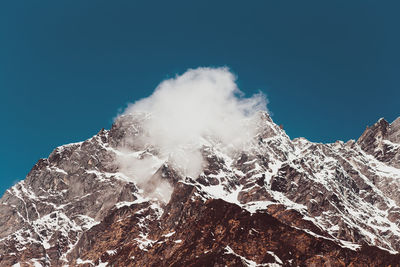 Low angle view of snowcapped mountain against clear blue sky