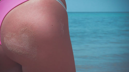 Close-up of heart shape made on skin with sand while standing by sea