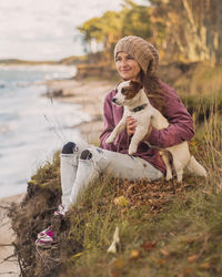 Full length of woman sitting on cliff with dog while looking away