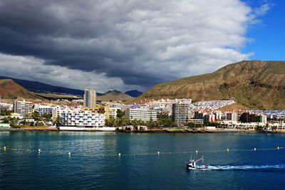 Buildings by sea against cloudy sky