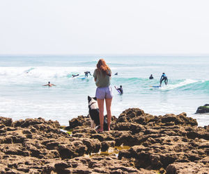 Rear view of friends on rock at beach against sky