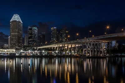 Illuminated buildings by river against sky at night