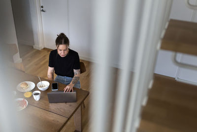 High angle view of young businesswoman using laptop while telecommuting at dining table