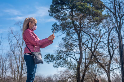 Cropped view of an adult woman with face mask and sunglasses taking a picture in a park