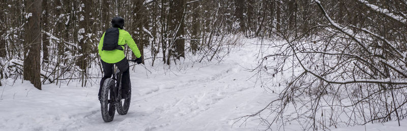 Rear view of man cycling on snow covered land