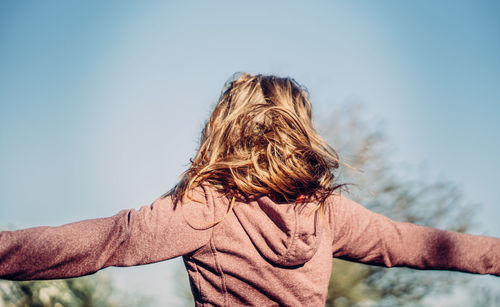 Rear view of woman with arms raised against clear sky