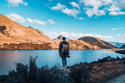 Rear view of man looking at lake against sky