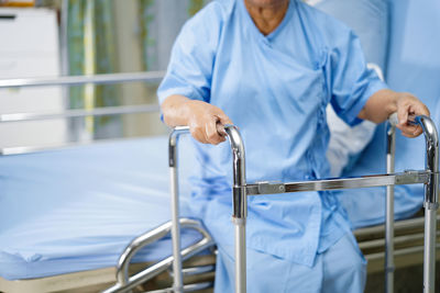 Midsection of person with mobility walker sitting on bed in hospital