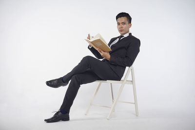 Young man sitting on chair against gray background