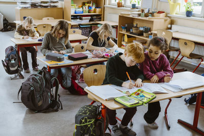 Male and female students studying together sitting at desk in classroom