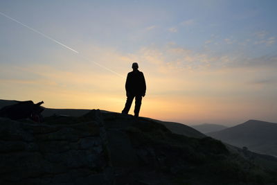 Silhouette man standing on mountain peak against sky during sunset