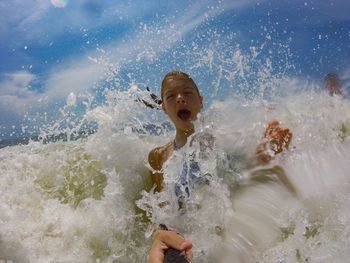 Portrait of teenage boy amidst splashed sea waves