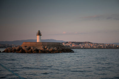 Lighthouse by sea and buildings against sky