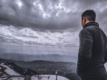 Rear view of man standing on mountain against sky