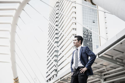 Businessman with hands on hip looking away while standing in city