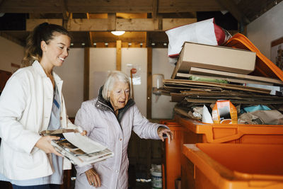 Smiling female nurse with wastes standing by senior woman in storage room