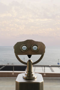 Close-up of coin-operated binoculars against sea during sunset