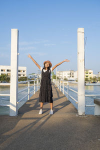 Full length portrait of young woman standing on walkway against sky