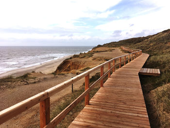 Boardwalk leading towards sea against sky