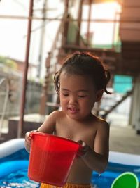 Shirtless cute girl holding bucket while standing in wading pool