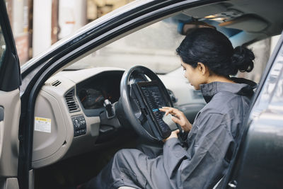 Side view of female mechanic using digital tablet while sitting in car