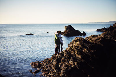 Rear view of woman standing on rock by sea against sky