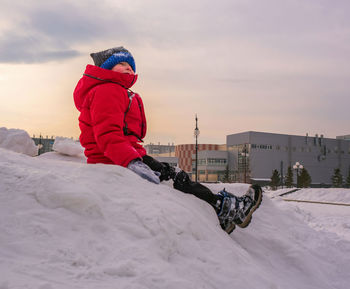 Smiling caucasian child casual wearing is sitting evening on a huge snow drift. 