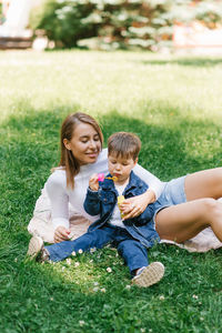 Beautiful cute young mom with her cute little son having fun sitting on the grass in the park