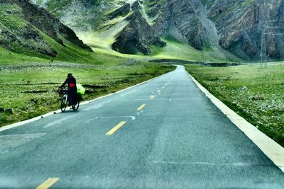 Man walking with bicycle on country road against mountain