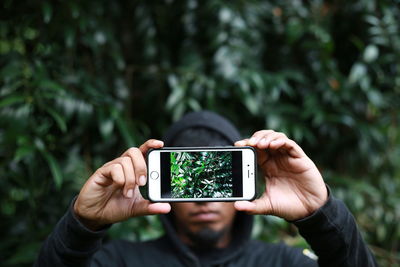 Close-up of hand holding smart phone against trees