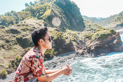Young woman on rock by sea against mountain