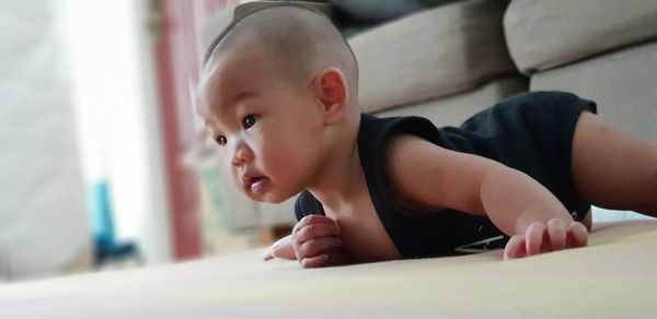 Cute boy looking away while relaxing on bed at home