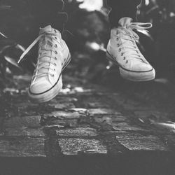 Low section of person wearing shoes while jumping on cobbled footpath