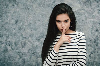 Portrait of beautiful woman standing with finger on lips against gray wall