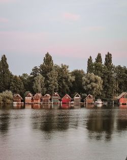 Houses by river against buildings and trees against sky