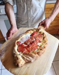 Midsection of man holding pizza on cutting board