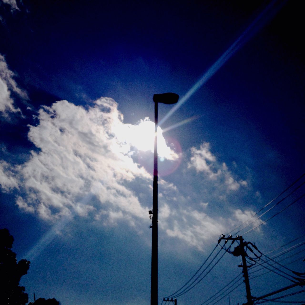 low angle view, electricity, sky, power line, street light, electricity pylon, lighting equipment, power supply, blue, connection, silhouette, cable, sun, cloud - sky, fuel and power generation, technology, pole, sunlight, sunbeam, cloud