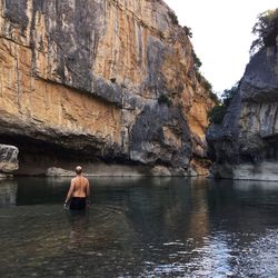 Rear view of man standing on cliff by sea