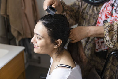 Mother combing hair of daughter with paraplegia in bathroom at home