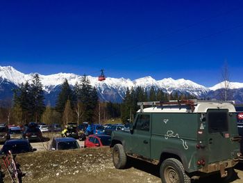 Vehicles on field against snowcapped mountains and blue sky during sunny day