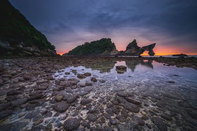 Rock formation in sea against sky during sunset