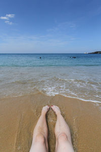 Low section of person on beach against sky