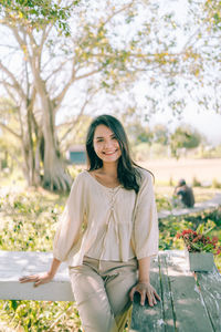 Portrait of smiling young woman standing against trees