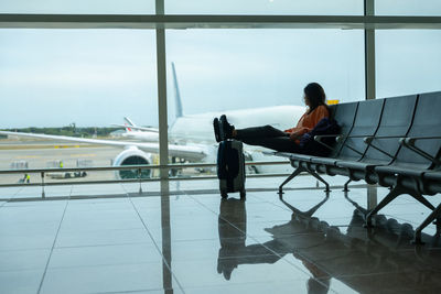Woman with her feet on her suitcase, waiting for her flight at the airport.